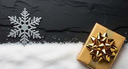Luxury gold gift box and glittery snowflake on dark slate background with white snow, flat lay composition.