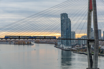 Naklejka premium Suspension Bridge Train Crossing Over Fraser River With Modern Vancouver Skyline At Sunset