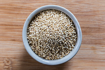 Top-down view of a ceramic bowl filled with whole white sorghum grains. A nutritious, gluten-free ancient grain and superfood ingredient on a rustic wooden background.