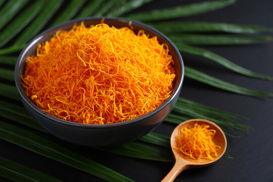 Bowl of Foi Thong a Thai dessert made from egg yolks boiled in syrup on dark surface with palm leaf