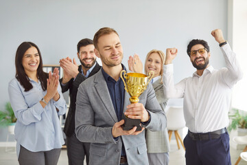 Happy businessman won prize or trophy, being acknowledged by friendly coworkers, holding golden...