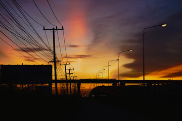 Silhouette of electric poles, power lines, billboards, elevated roads in sunset.