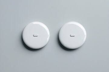 Two identical, glossy white, round buttons/switches on a light gray surface