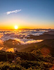 A breathtaking landscape captures a vibrant sunset over rolling mountain ridges enveloped in a sea of clouds. Rays of light pierce the dense atmosphere
