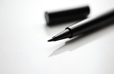 Fototapeta premium Black liquid eyeliner pen with cap detached rests on white surface. Fine tip for precise line drawing makeup application. Beauty product macro.
