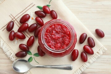 Homemade preserved  jam from Cornelian cherry dogwood, lat. Cornus mas macrocarpa,  in a jar. Fresh berries on embroidered napkin, flat lay.
