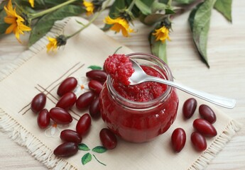 Homemade preserved  jam from Cornelian cherry dogwood, lat. Cornus mas macrocarpa,  in a jar. Fresh berries on embroidered napkin.