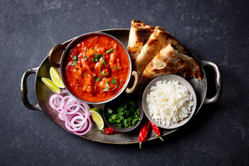 Authentic Indian feast: chicken tikka masala with rice, naan, lime and spices. Grey background. Top view.