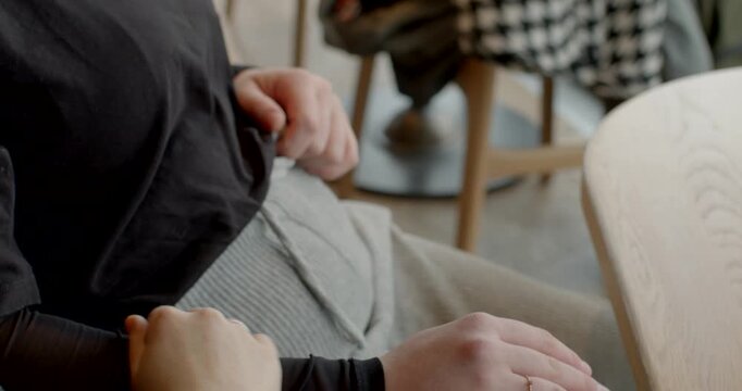 white women seated cafe holding hands, close-up hands resting on knee and armrest, bride comforted by friend with subtle engagement ring, warm wood table and soft daylight, intimate supportive moment