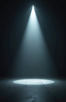 Strong white spotlight shines on empty dark stage floor. Bright light beam creates dramatic cone effect with atmospheric haze. Focused illumination highlights plain concrete surface. Suggests