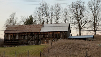 Old wooden barn with trees and blue sky in autumn