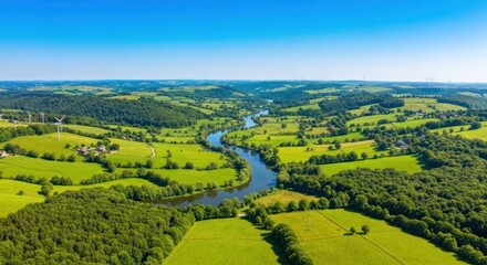 Obraz premium Panoramic view of lush green valley with river snaking through rolling hills under a blue sky