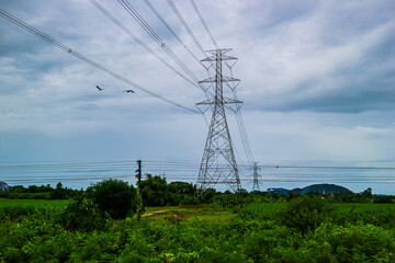 Striking high-voltage transmission tower against a dramatic, cloudy sky, surrounded by lush green...