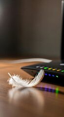 Close-up of a white feather resting on a wooden desk next to a modern electronic device with colorful indicator lights in a well-lit workspace