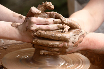 The potter's wheel to turn. The pupil and the master the hands give to a piece of clay the cylindrical form.
