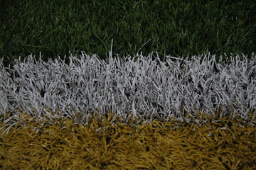 Close-up of artificial turf with green, white, and yellow sections. Ideal for sports, field design, or texture-themed visual content