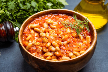 Baked bean dish in wooden bowl on black background.	