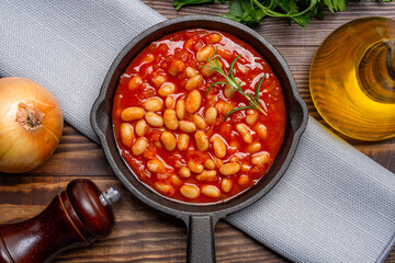 Baked bean dish in cast iron pan on wooden background.	