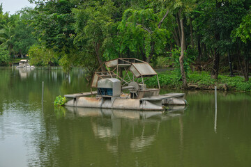 Obraz premium Small wooden hut near a lake surrounded by green trees. Represents rural lifestyle, relaxation, and outdoor leisure