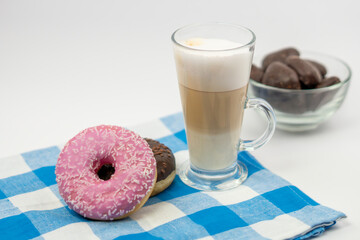 Latte coffee with two donuts and gingerbread in a bowl placed on a blue kitchen cloth