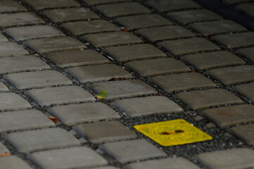Yellow guiding stone, Vivid yellow indicator aiding pedestrian movement across uneven stones, Colorful tactile strip provides guidance on weathered cobblestone walkways for pedestrians