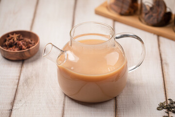 Warm milk tea brewed with star anise and cinnamon served in a clear glass teapot on wooden table