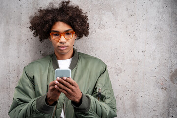 Serious African American man with piercing in nose in red glasses holding mobile phone
