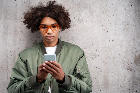 Serious African American man with piercing in nose in red glasses holding mobile phone