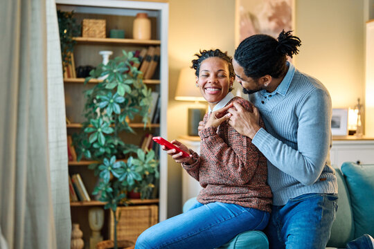 Happy young couple having fun using smartphone during oline video call conversation or shopping or using an app at home