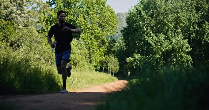 Athlete, man and running for fitness in woods with exercise, cardio training and morning routine. Person, check watch and jog in forest for endurance workout, low angle and improve stamina in nature