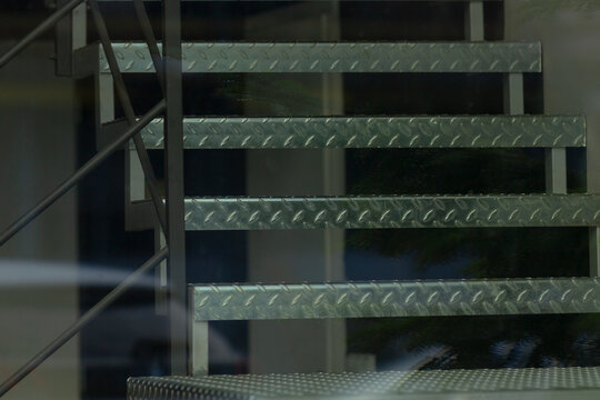 metal staircase reflected through glass facade, textured diamond plate treads and steel stringers visible
