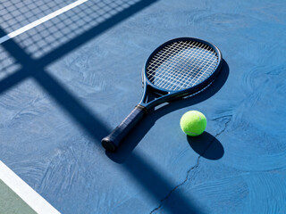 Tennis racket and ball on blue court with net shadow pattern