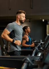 Fototapeta premium Portrait of a young man and a black woman exercising in a gym, running using thereadmill machine equipment, healthy lifestyle and cardio exercise at fitness club concepts