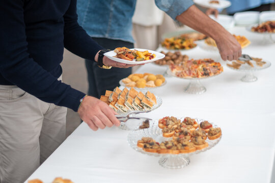 Diverse group of friends and colleagues enjoying a delicious buffet spread at a catered event with an assortment of appetizing finger foods and desserts