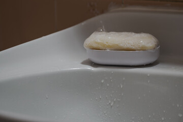 Soap bubbles on an oval soap bar on a white plastic tray in the sink.
