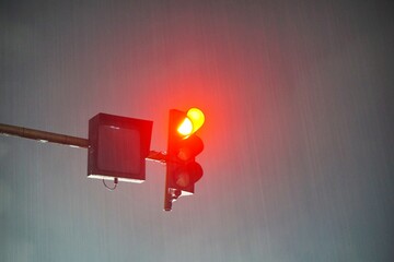 Red traffic light glowing brightly during a rainy night.