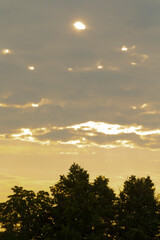Fototapeta premium The bright sun is shining beautifully through the fluffy clouds that are hovering above the majestic trees in the landscape