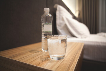Glass and bottle of water on a bedside table in a cozy bedroom, symbolizing hydration, wellness, and post-workout recovery in a calm self-care setting.