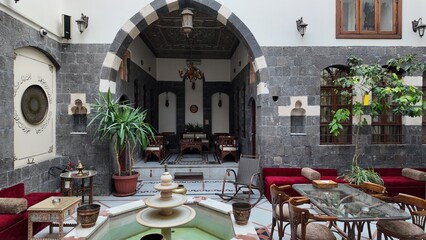 Traditional Middle Eastern courtyard with a classic liwan design in an old Arabic house. The scene highlights stone arches, decorative pillars, and a spacious central seating area, reflecting authenti