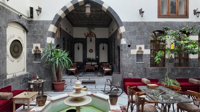 Traditional Middle Eastern courtyard with a classic liwan design in an old Arabic house. The scene highlights stone arches, decorative pillars, and a spacious central seating area, reflecting authenti