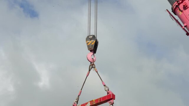 Crane machine is lifting heavy object using the spreader bar on cloudy sky background. Industrial operation scene and equipment object.