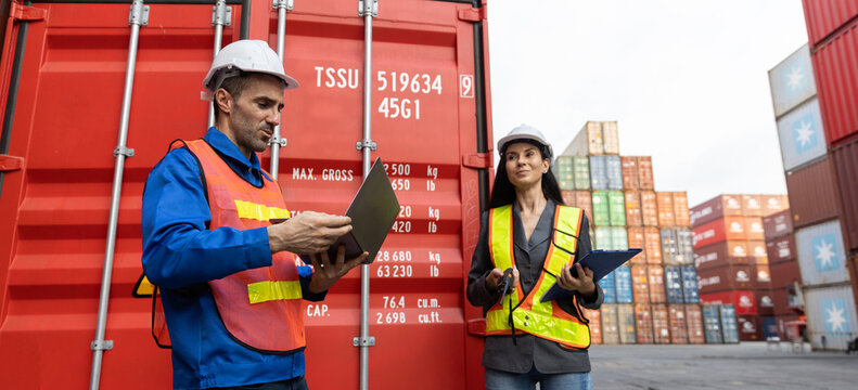 Two cargo inspectors, man and woman, stand confidently beside large shipping containers, reviewing logistics data and planning operations with serious and focused expressions