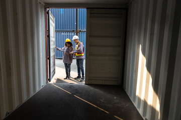 Two logistics workers in safety gear inspecting and discussing inside a shipping container at a port terminal. Concept of supply chain, cargo inspection, warehouse, freight, and shipping industry.