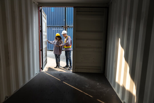 Two logistics workers in safety gear inspecting and discussing inside a shipping container at a port terminal. Concept of supply chain, cargo inspection, warehouse, freight, and shipping industry.