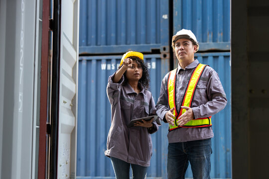 Two logistics workers in safety gear inspecting and discussing inside a shipping container at a port terminal. Concept of supply chain, cargo inspection, warehouse, freight, and shipping industry.