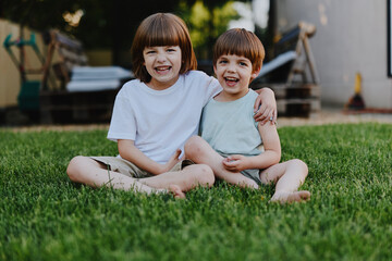 Fototapeta premium Happy children smiling on green grass, enjoying a sunny day together. This cheerful moment captures the joy of childhood and friendship in a natural setting.