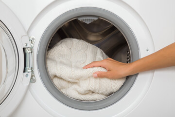 Young adult woman hands holding and unloading white warm soft sweater from opened washing machine. Delicate knitted clothes care. Closeup. Front view.