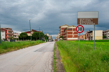 Panorama. Paesaggio di strada che entra in piccolo paese del meridione rurale tra verdi campi verso antiche case. Puglia, natura Italia.