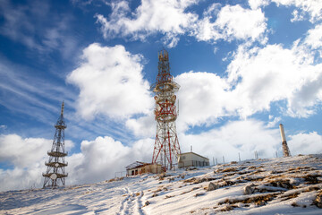 Telecommunication towers on a snowy mountain peak under a bright blue sky, showing modern infrastructure, wireless technology, and winter landscape scenery.