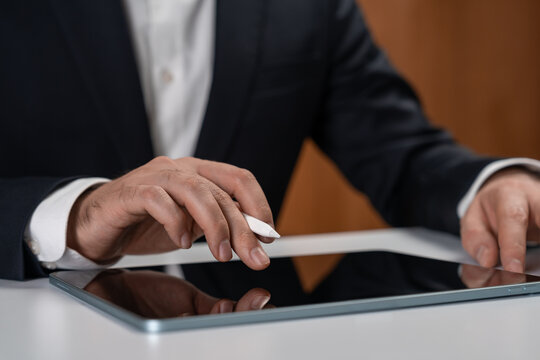 Businessman using digital pen and tablet at office desk, close-up of hands interacting with modern gadget in professional setting, technology concept..